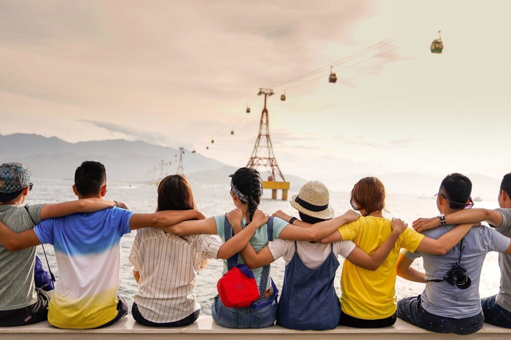 Several friends sitting with hands on each other's shoulders, facing the sea, with mountains in the distance