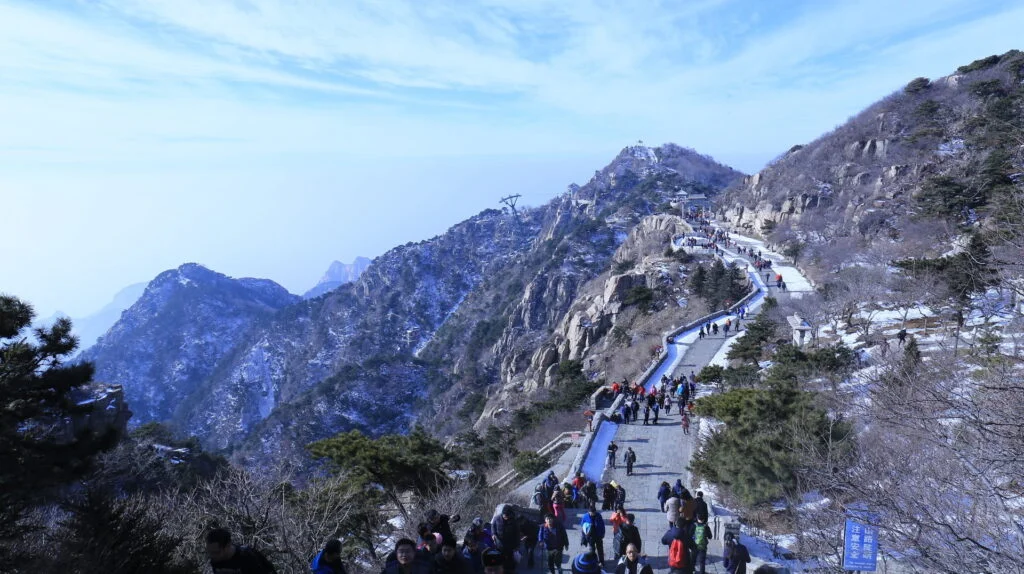 Scenic view of Taishan Mountain, with a clear blue sky and fluffy white clouds, as people embark on a challenging uphill hike