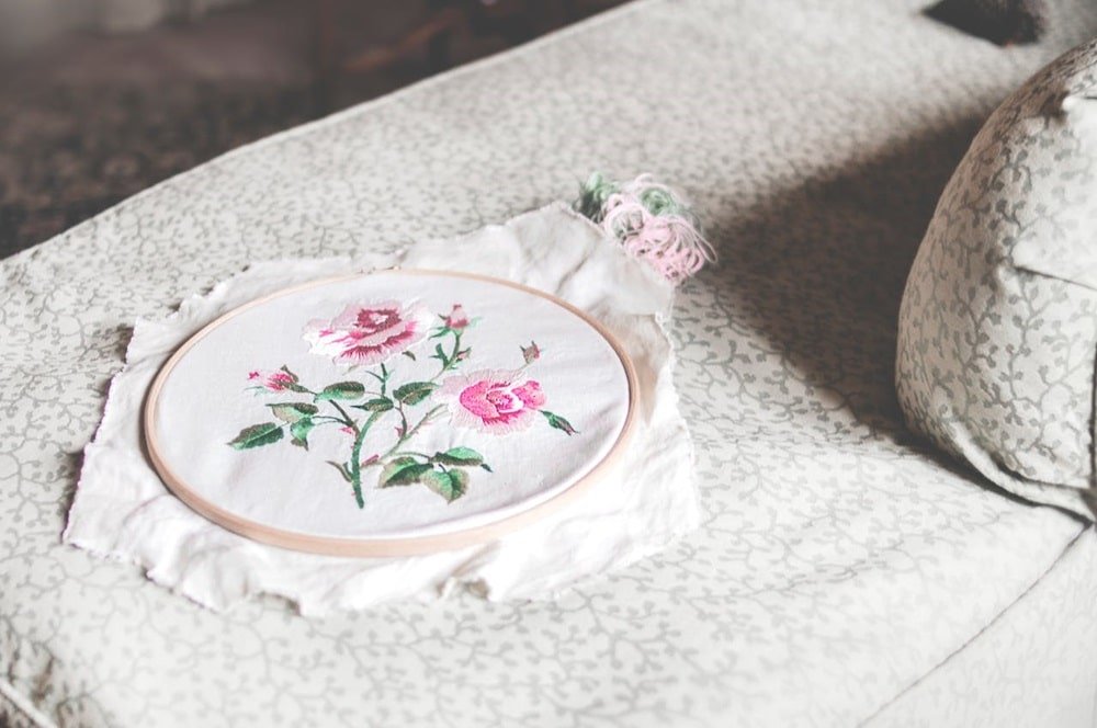 There is a completed embroidery piece of a pink flower on the table
