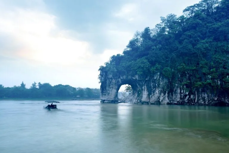 Elephant Trunk Hill on the right side with a person on a bamboo raft floating on a green lake