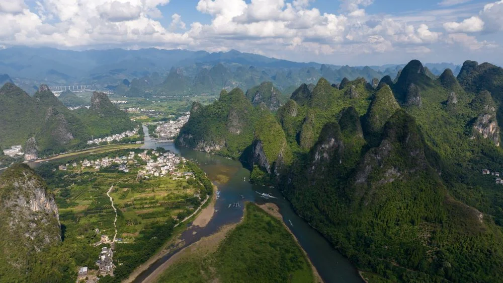 Aerial shot of Yulong River with clear views of karst mountains, fields, and houses along the riverbanks