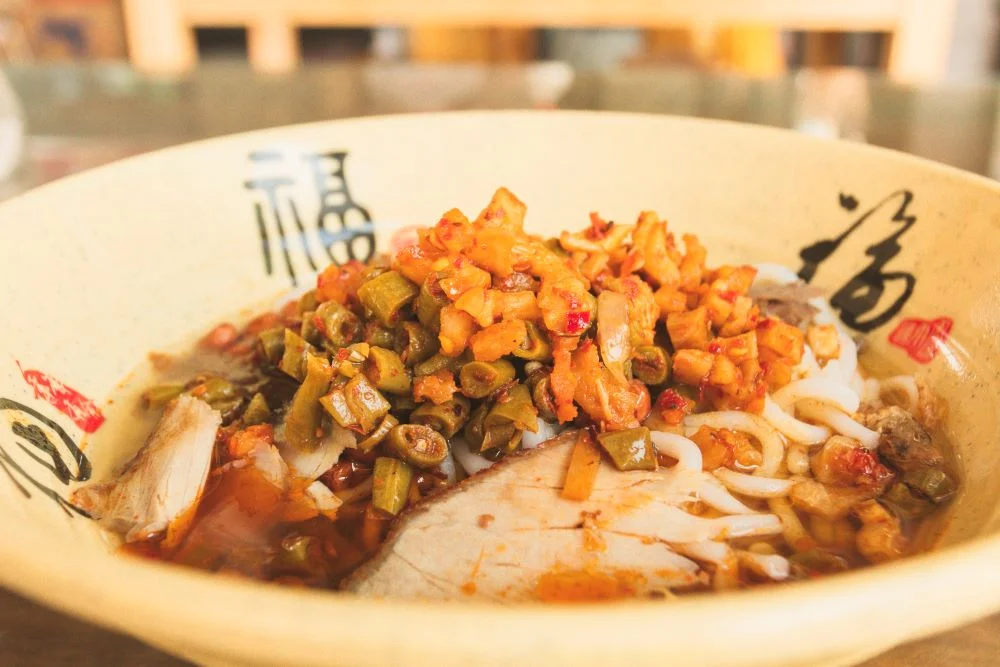 Bowl of Guilin rice noodles with pickled beans, radish, and meat slices