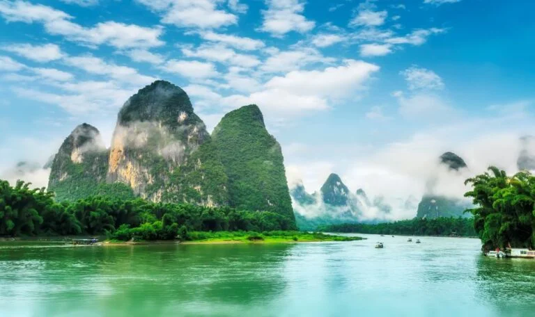 Misty karst mountains and green lake under blue skies