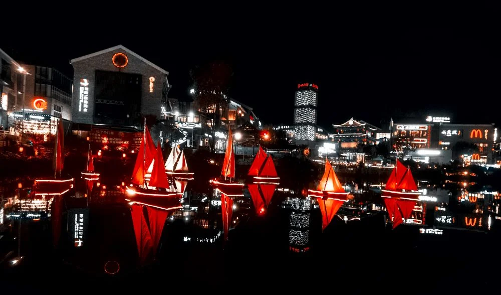 Night view of Yangshuo West Street with illuminated buildings and boats cruising on the river