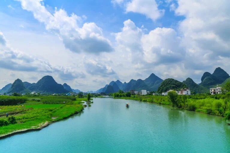Wide Yulong River with picturesque fields, houses, and distant karst mountains under a beautiful sky