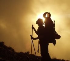 A man carrying a mountaineering bag climbs to the top of the mountain facing the sunset - 300